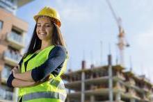 身穿安全背心、头戴安全帽的女工程实习生站在建筑工地前